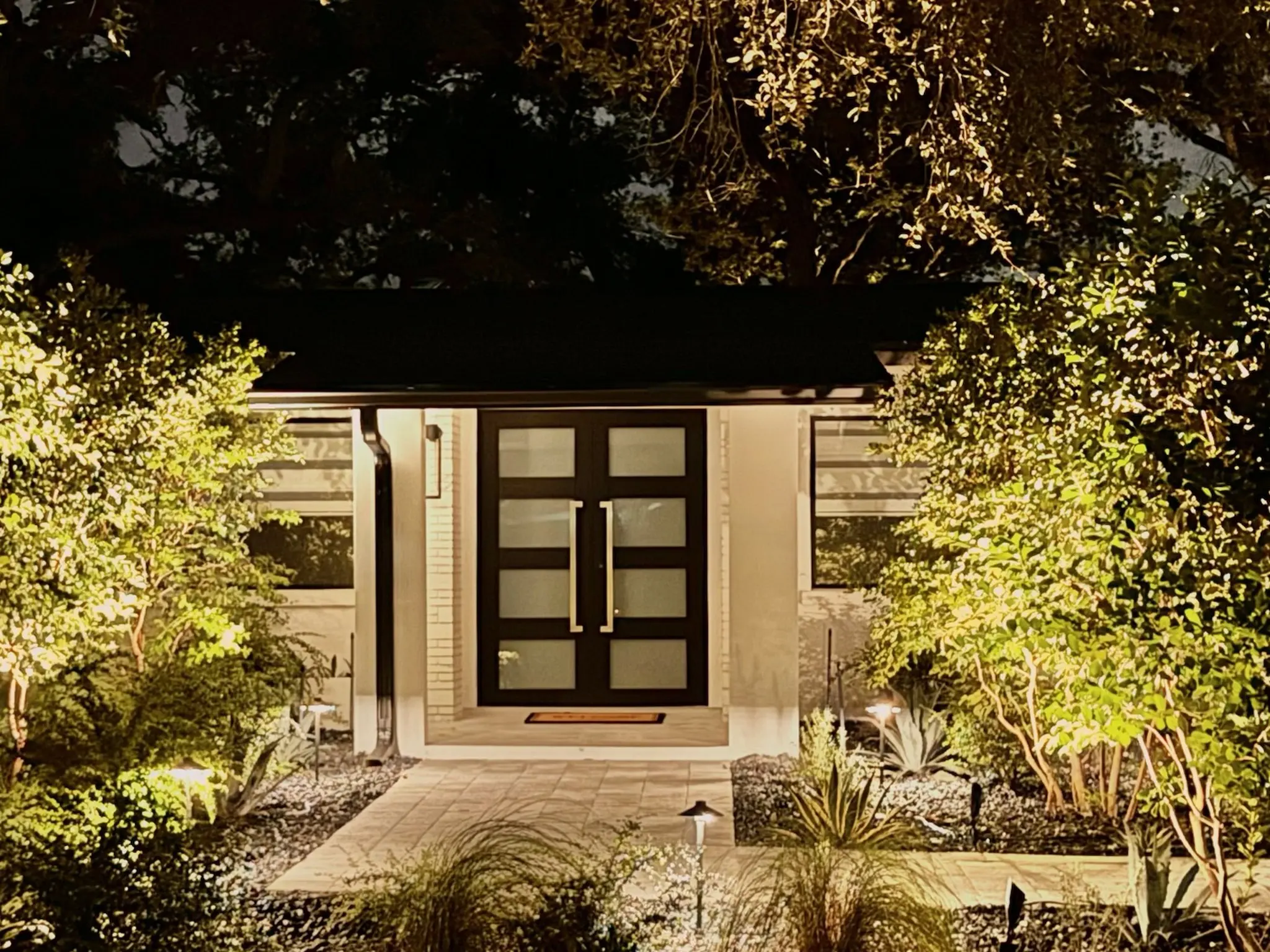 After: renovated home exterior with modern black double doors and landscape lighting