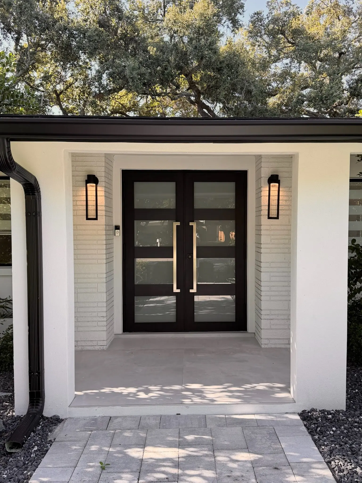 Renovated front entry with modern black double doors, wall sconces, and paver walkway