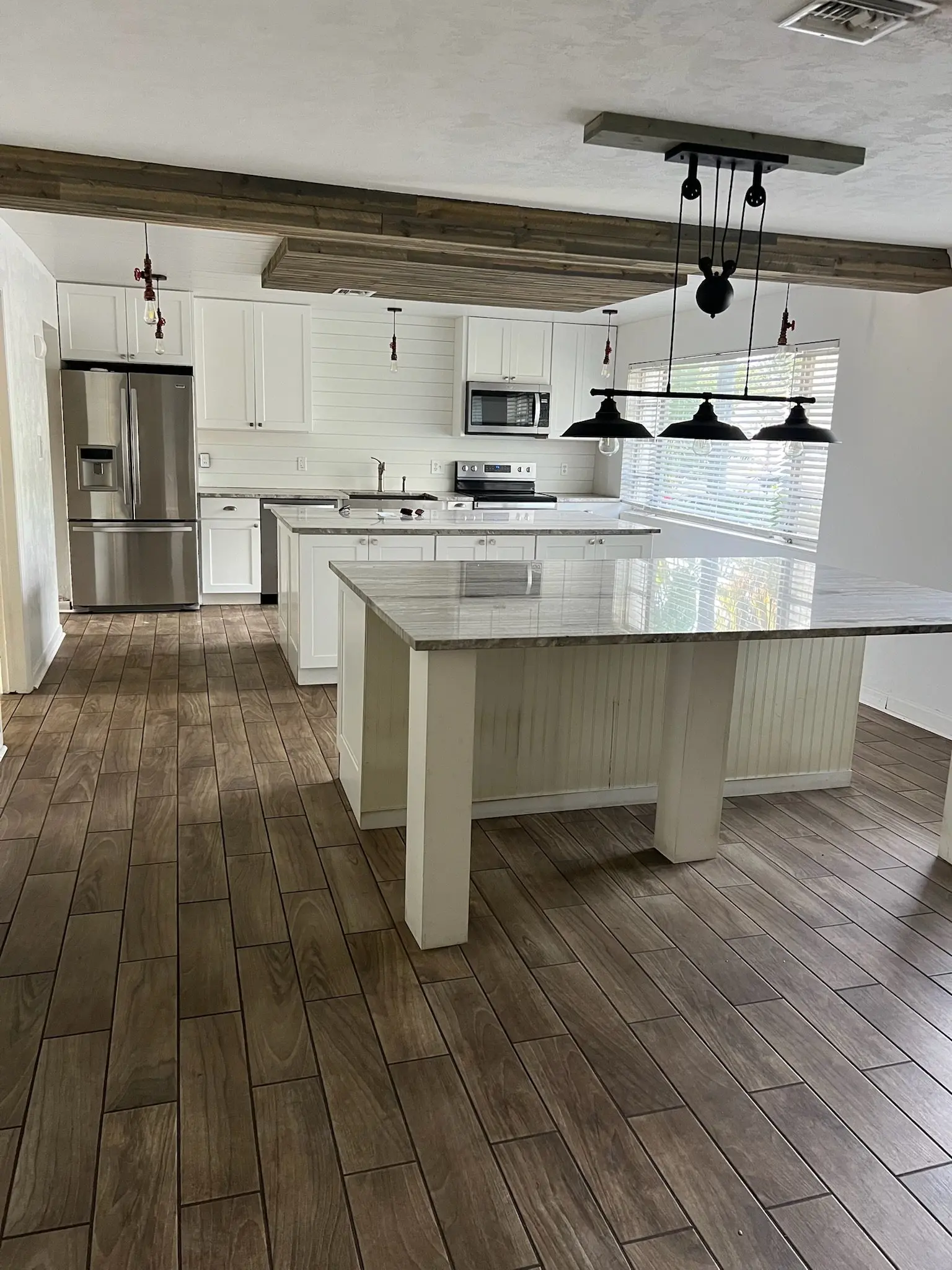 Kitchen remodel with white shaker cabinets, a large quartz island, and wood-look tile floors