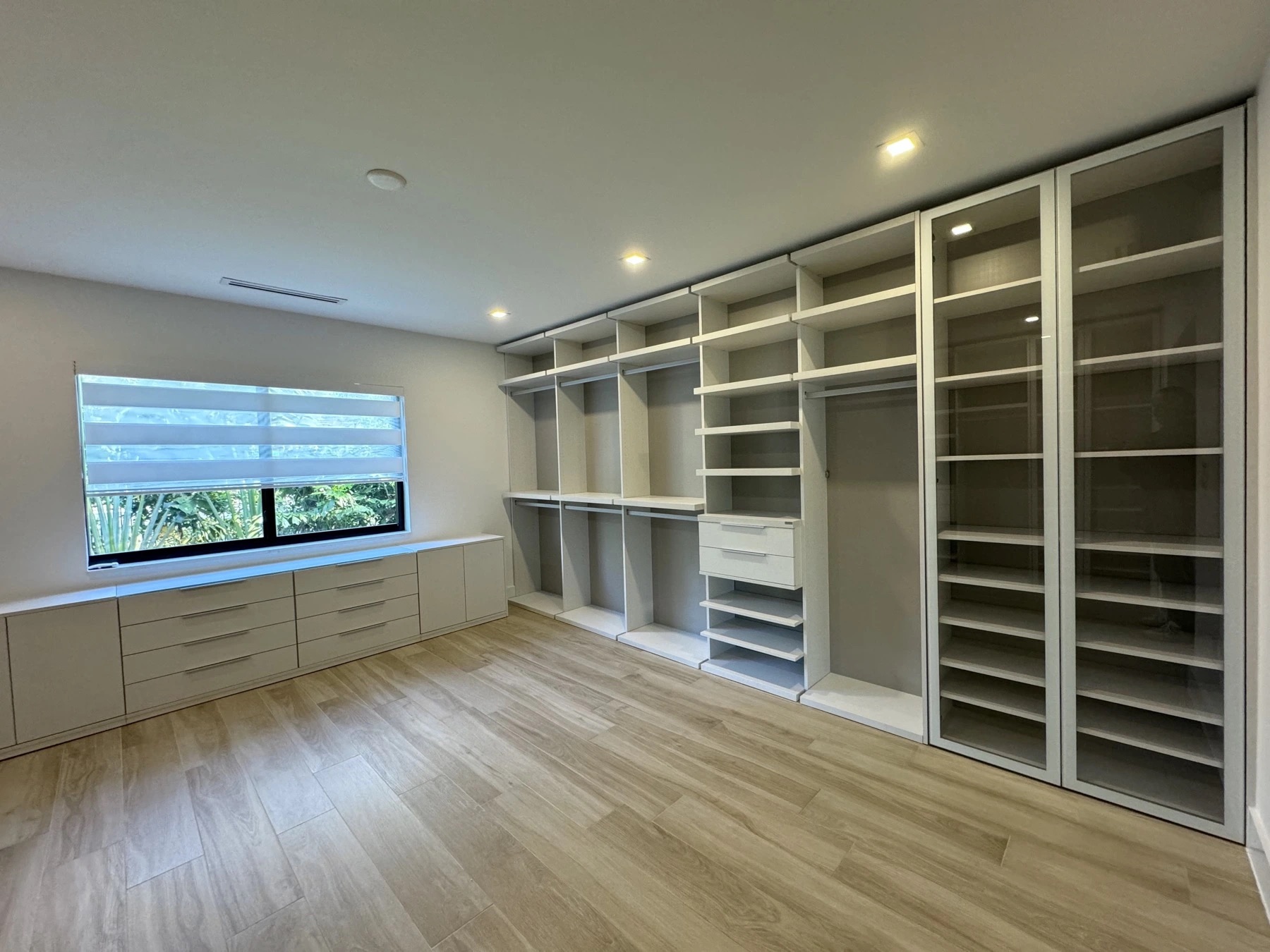 Custom walk-in closet in Fort Myers, FL built in an enclosed patio, with built-in shelving, hanging rods, drawers and glass-door display cabinets